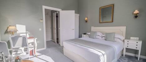 A bedroom with a large bed, bedside tables, a chair, a desk, and a chandelier.