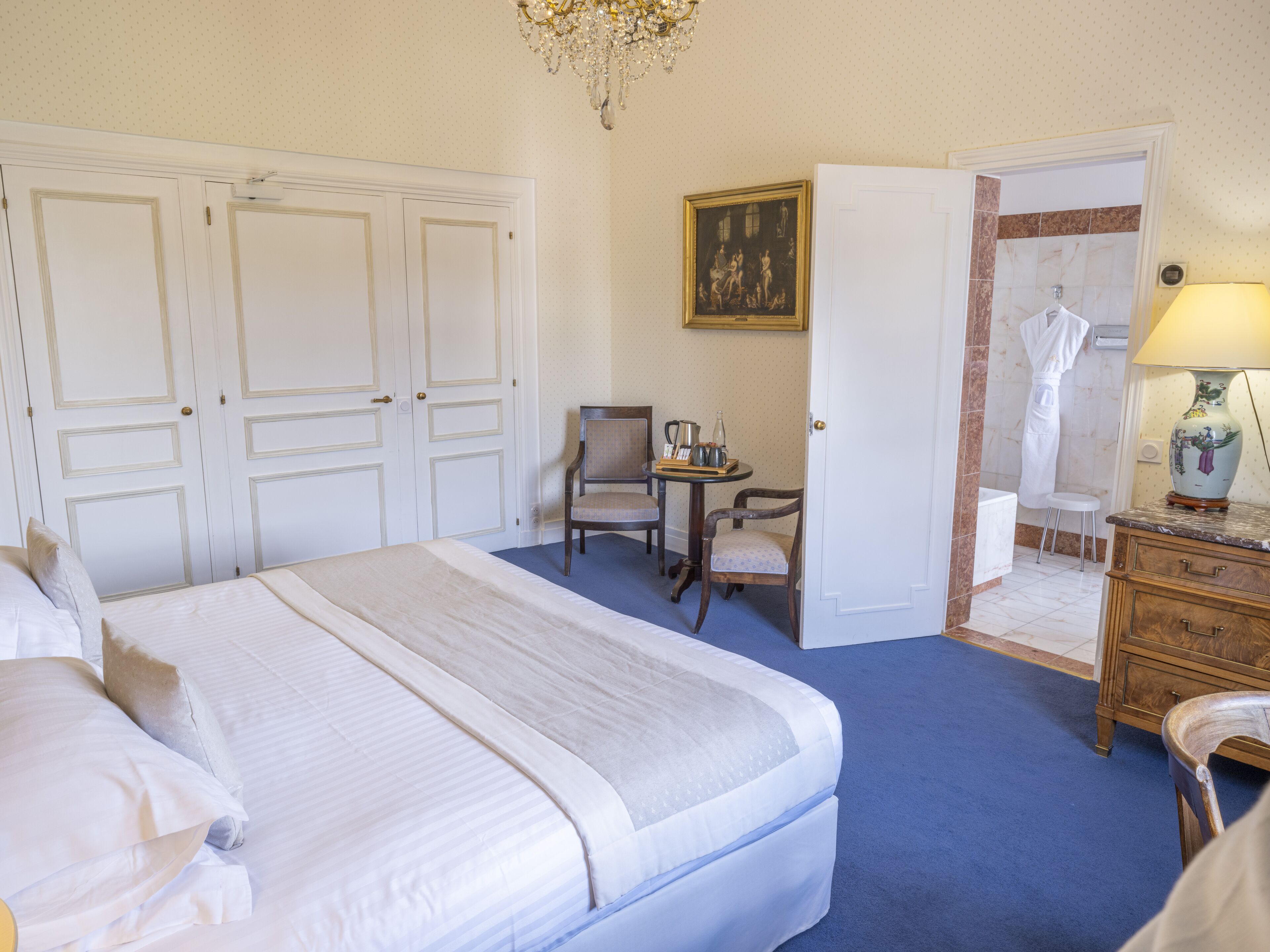 Habitación de hotel con una cama grande, un escritorio con silla, baño con bata y toalla, y un candelabro.