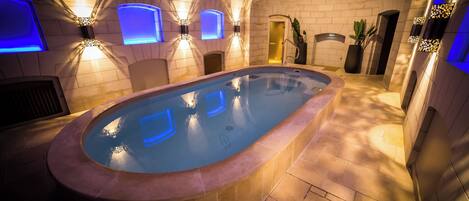 Un jacuzzi de diseño curvo, rodeado de paredes de azulejos y suelo de piedra.