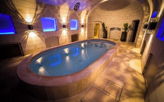 Uma piscina de spa com design curvo, rodeada por paredes revestidas de azulejos e piso de pedra.