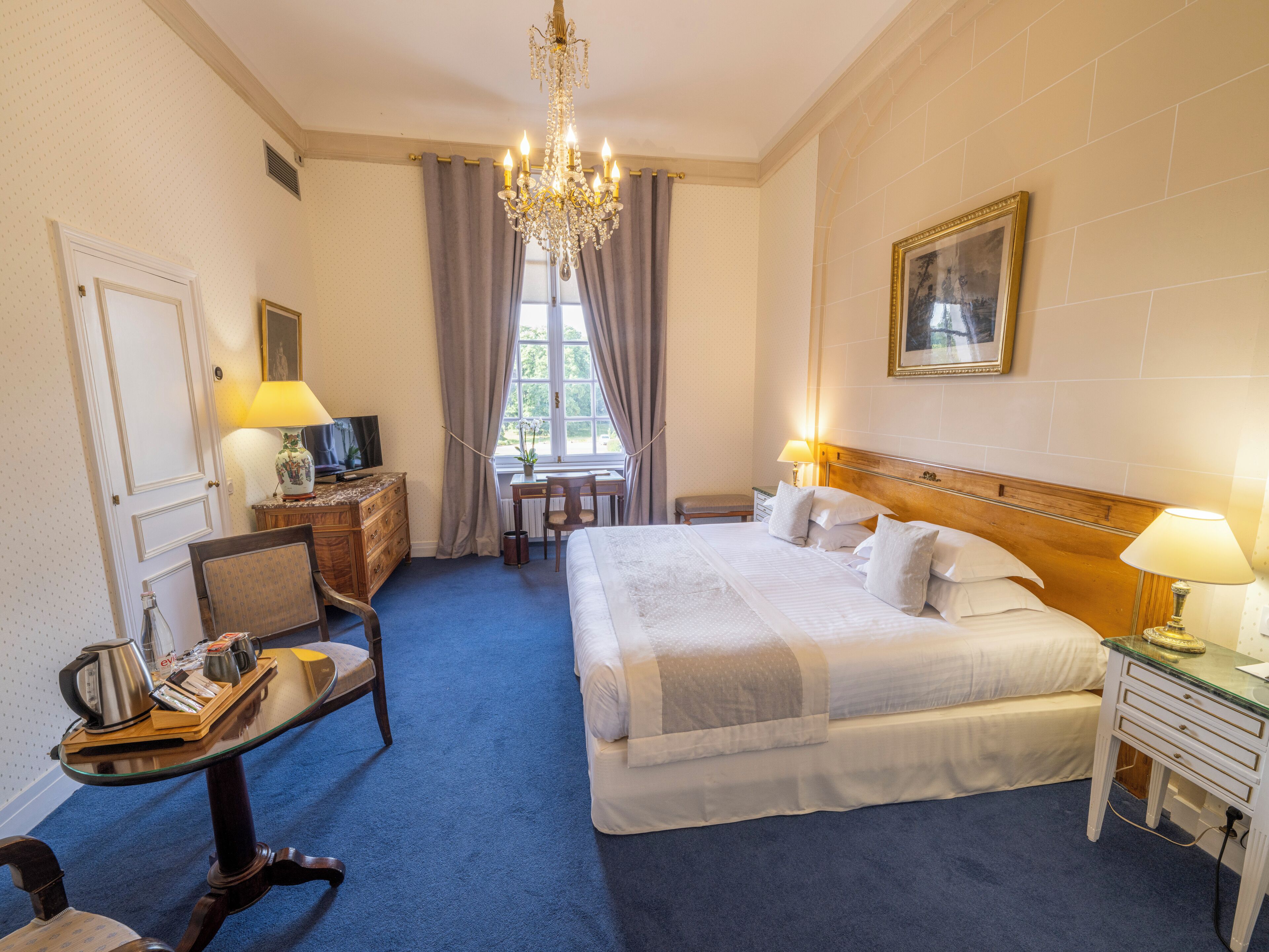 Ein Hotelzimmer mit einem großen Bett, einem Schreibtisch, einem Sessel, einem Fernseher und einer Kristallleuchter.