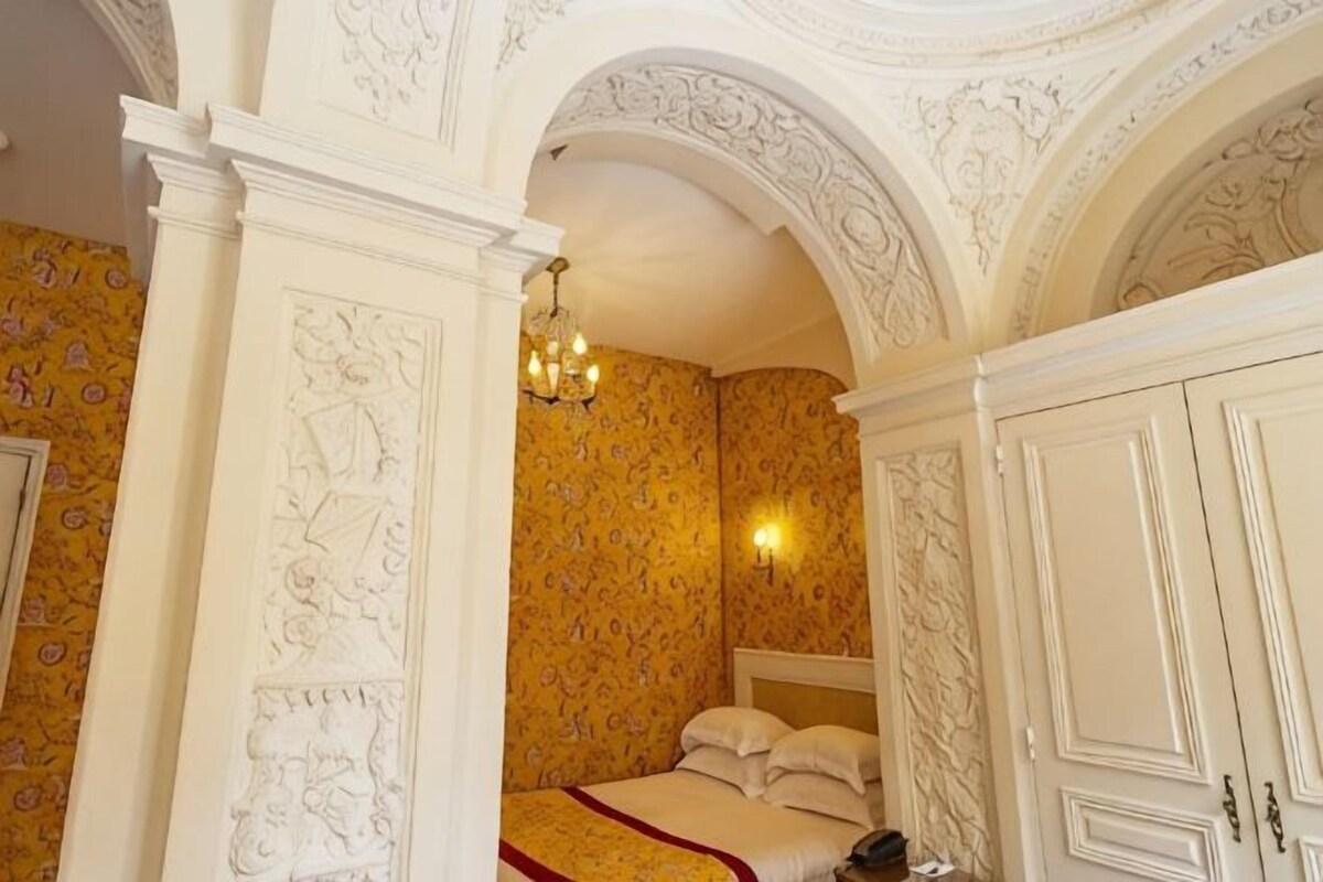A bedroom with a bed, a chandelier, and ornate ceiling details.