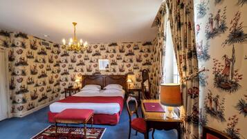 Habitación de hotel con una cama grande, una mesita de noche de madera, un escritorio con lámpara, una silla y una alfombra estampada.