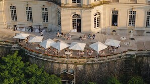 An outdoor café with tables and umbrellas, surrounded by stone walls and greenery. - Château d'Artigny (Montbazon)