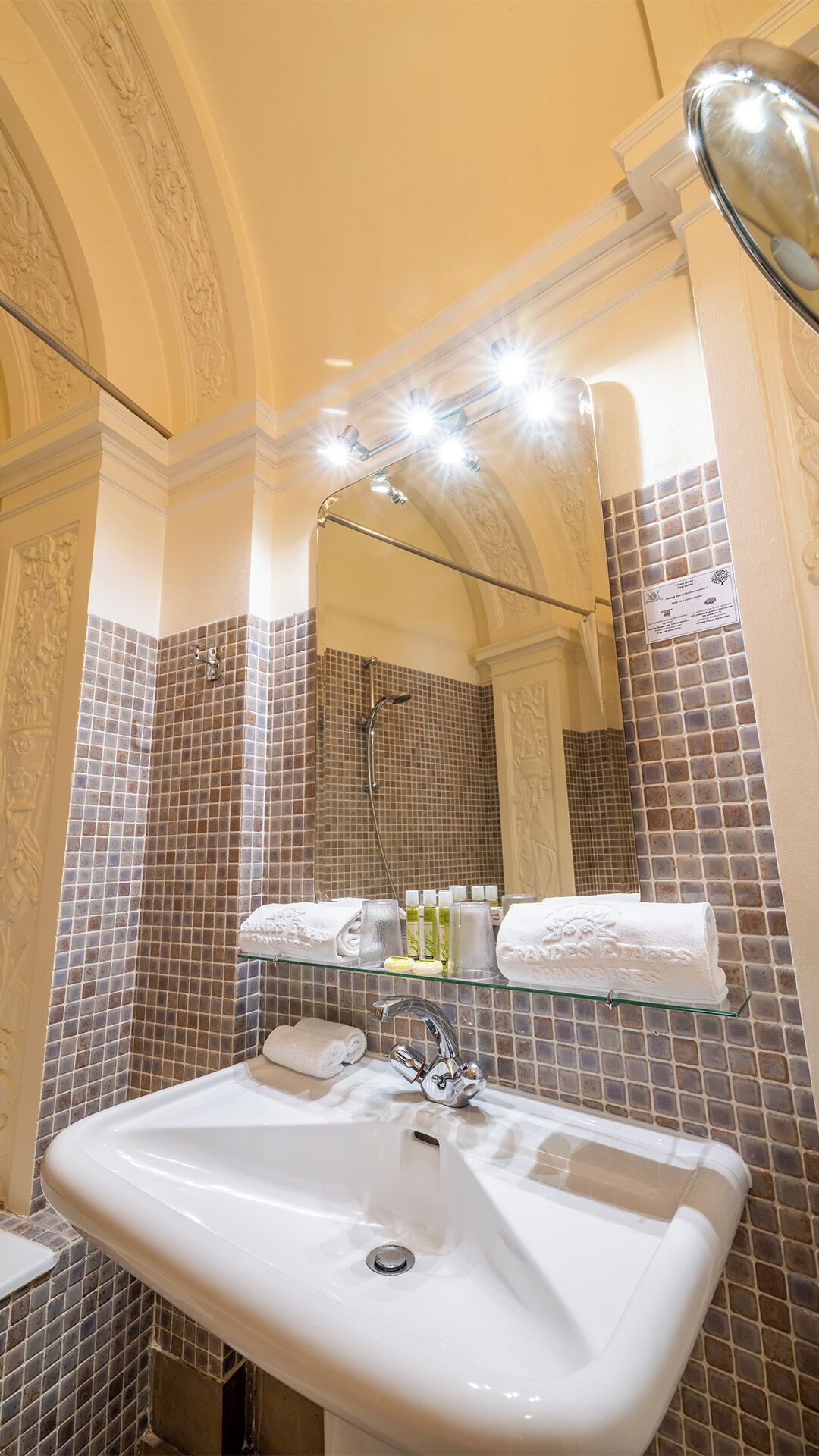 A bathroom with a white sink, a glass shelf with toiletries, and a mirror above the sink.