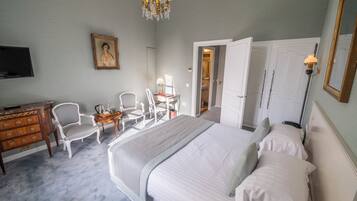 A bedroom with a large bed, a desk with a chair, a dresser, a television, and a chandelier.