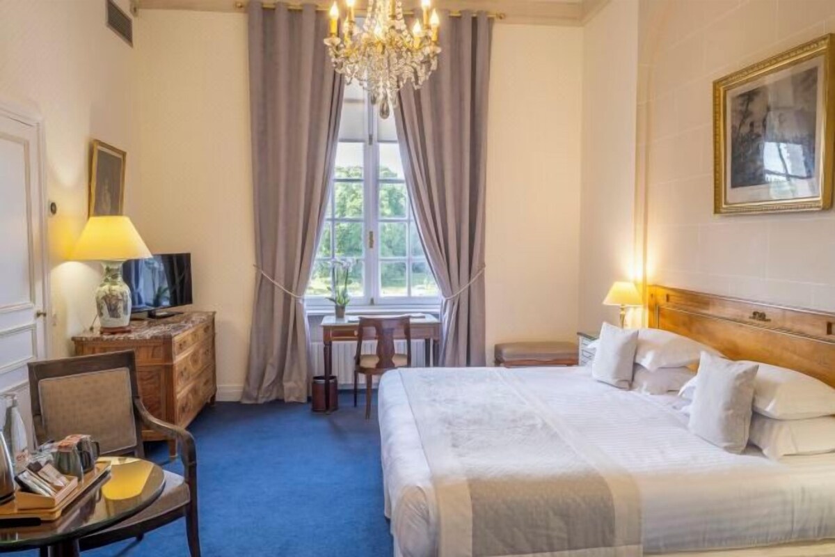 A hotel room with a large bed, a desk with a lamp, a chair, a dresser, and a television.