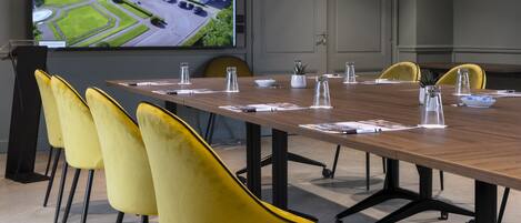 A conference room with a long table, yellow chairs, and a large screen displaying an aerial view of a building.