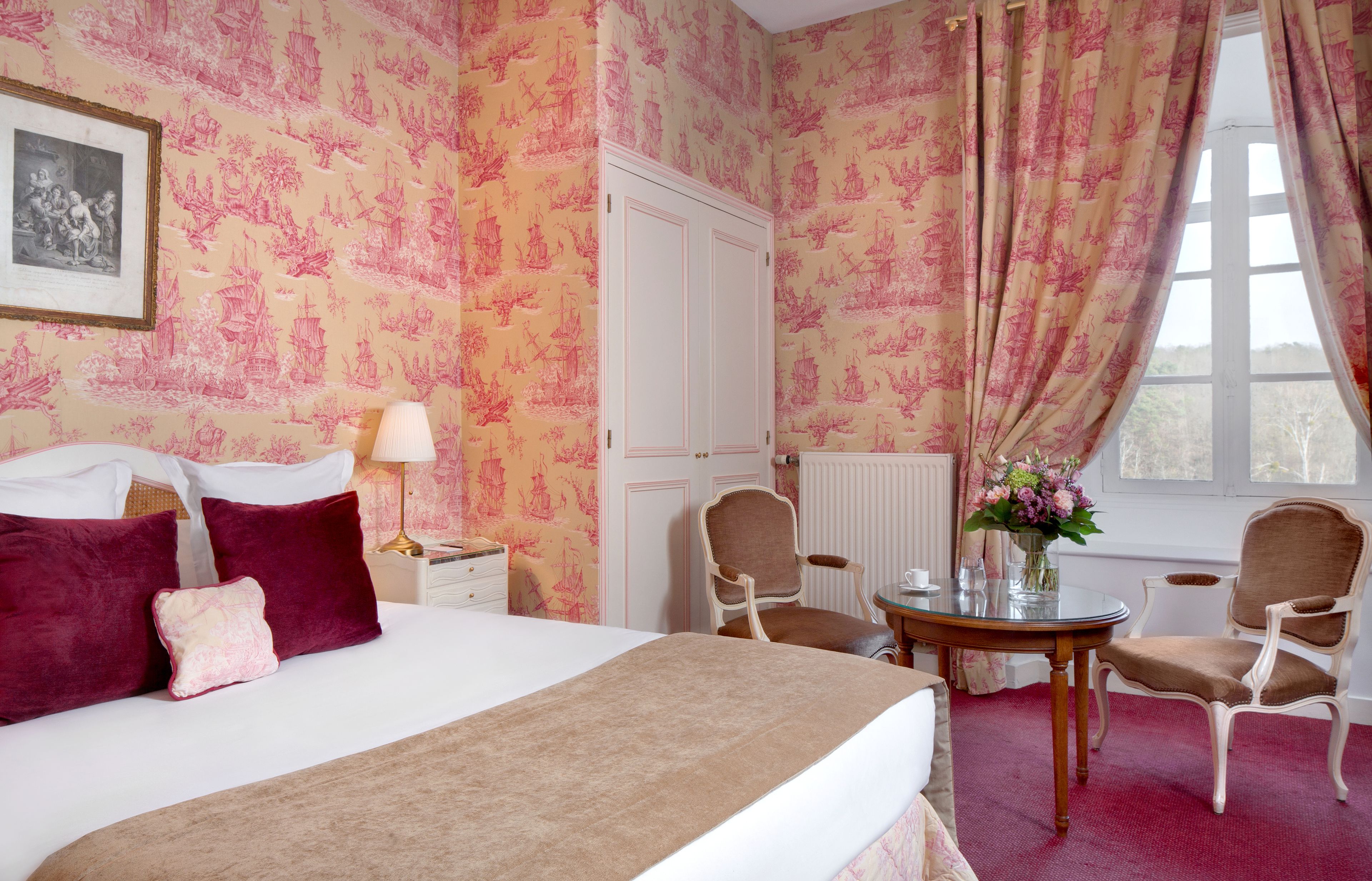 Ein Hotelzimmer mit einem großen Bett, zwei Sesseln, einem kleinen Tisch und einem Fenster mit Vorhängen.