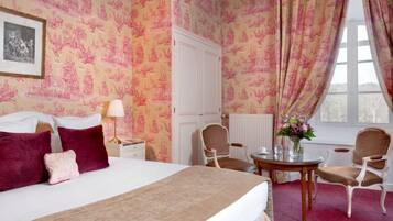 A hotel room with a large bed, two chairs, a small table, and a window with curtains.