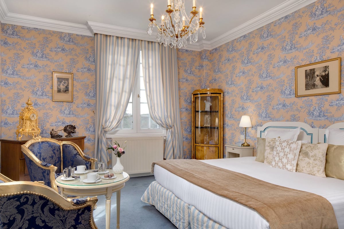 Ein Schlafzimmer mit einem großen Bett, einer Kristallleuchter, einem Holzschrank und einem Essbereich mit Tisch und Stühlen.