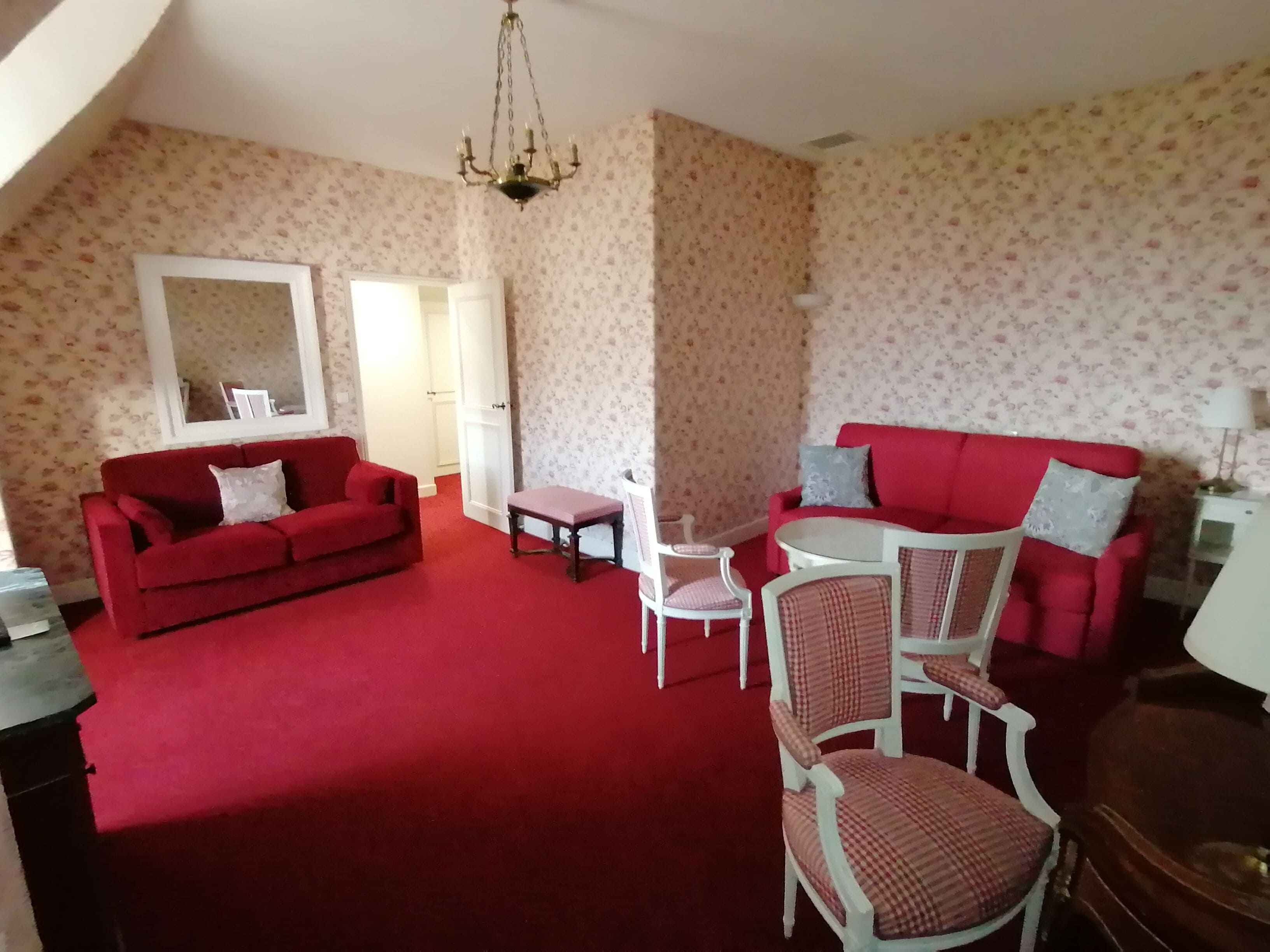 A living room with a red carpet, two red sofas, a small table, and a chandelier.