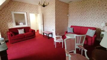 A living room with a red carpet, two red sofas, a small table, and a chandelier.