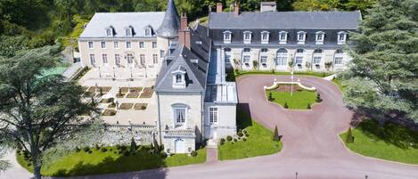 A large, historic building with a symmetrical facade, a central tower, and a formal driveway leading to the entrance.