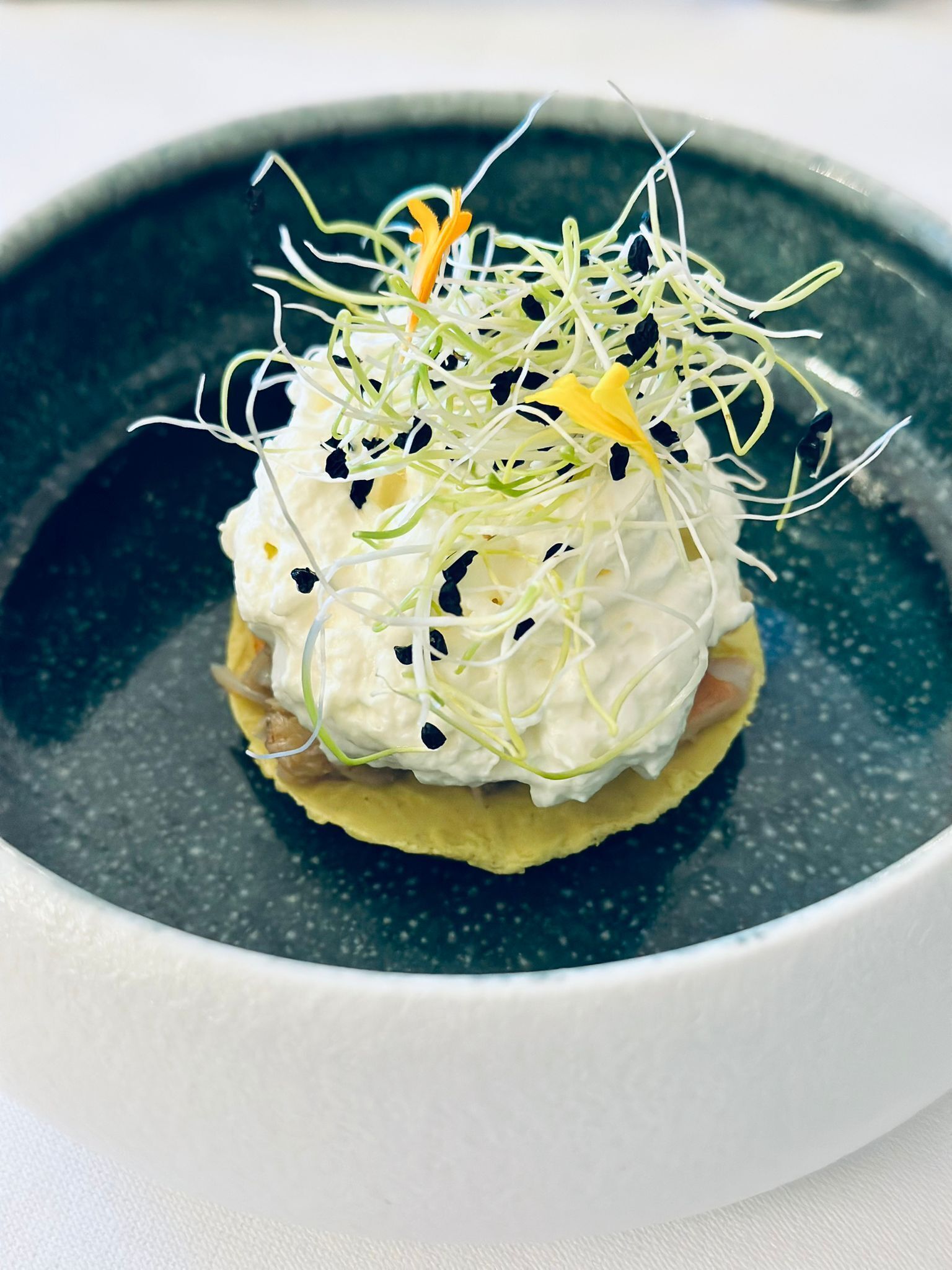 A dish with sprouts and a yellow flower on a plate.