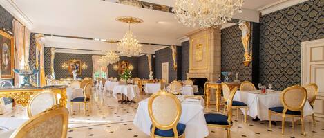 A luxurious dining room with ornate chandeliers, gold-accented furniture, and a polished marble floor.