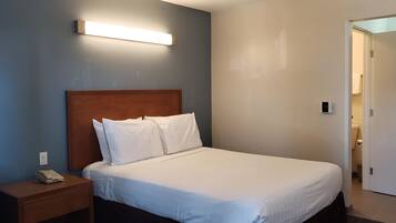 A hotel room with a single bed, a bedside table with a phone, and a wall-mounted light fixture.