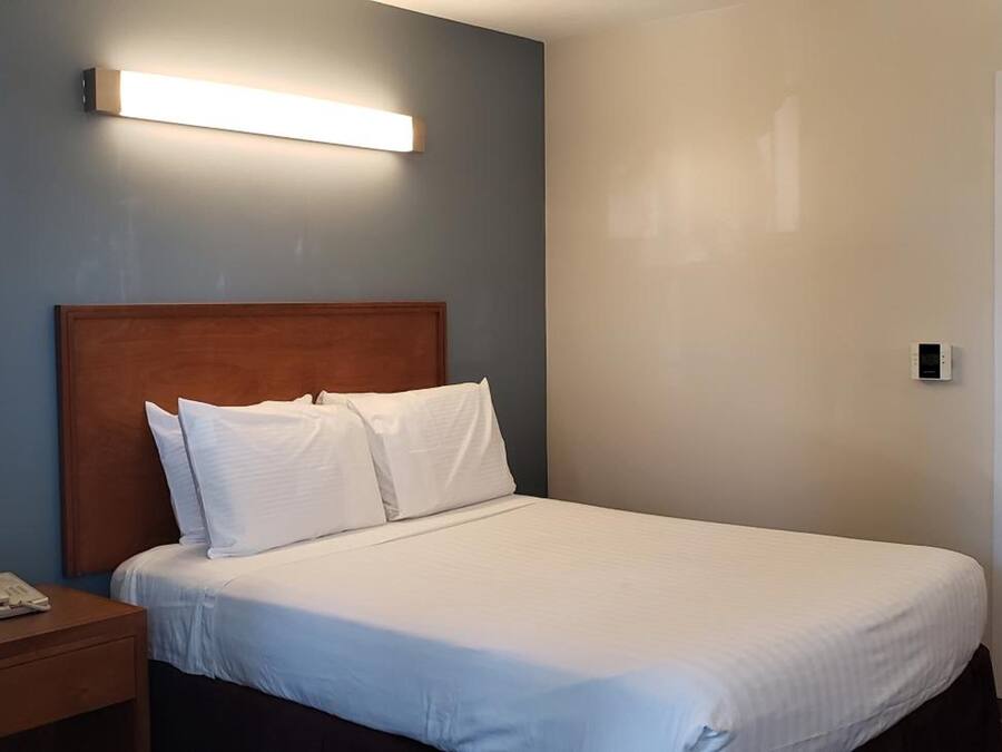 A hotel room with a single bed, a bedside table with a phone, and a wall-mounted light fixture.