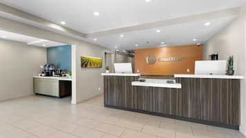 Un área de recepción con diseño moderno, un mostrador de recepción, una máquina de café y un televisor montado en la pared.