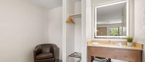 A modern bathroom with a wooden vanity, a large mirror, a towel rack, and a leather chair.