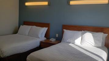 Habitación de hotel con dos camas, cada una con ropa de cama blanca y cabeceros de madera. Se observa una mesita de noche con un teléfono y una lámpara.