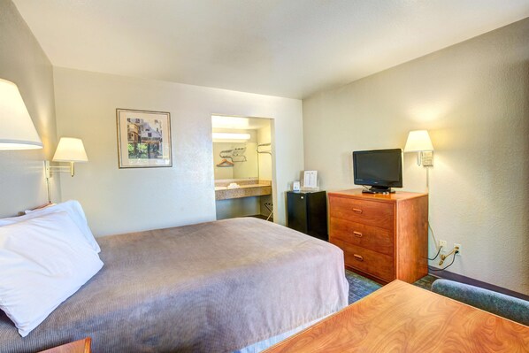 Una habitación de hotel con cama, escritorio, televisor, cómoda y espejo.