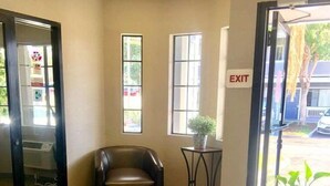A hotel lobby with a leather chair, a small table with a potted plant, and an exit sign. - Good Nite Inn Redlands (Redlands)