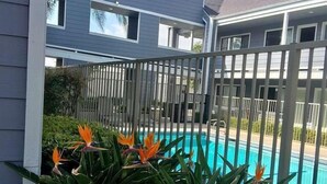 A residential pool area with a fenced deck, surrounded by tropical plants and a clear blue sky. - Good Nite Inn Redlands (Redlands)