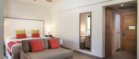 Una habitación de hotel con cama, sofá, mesa redonda, ventilador de techo, espejo y puerta de madera.
