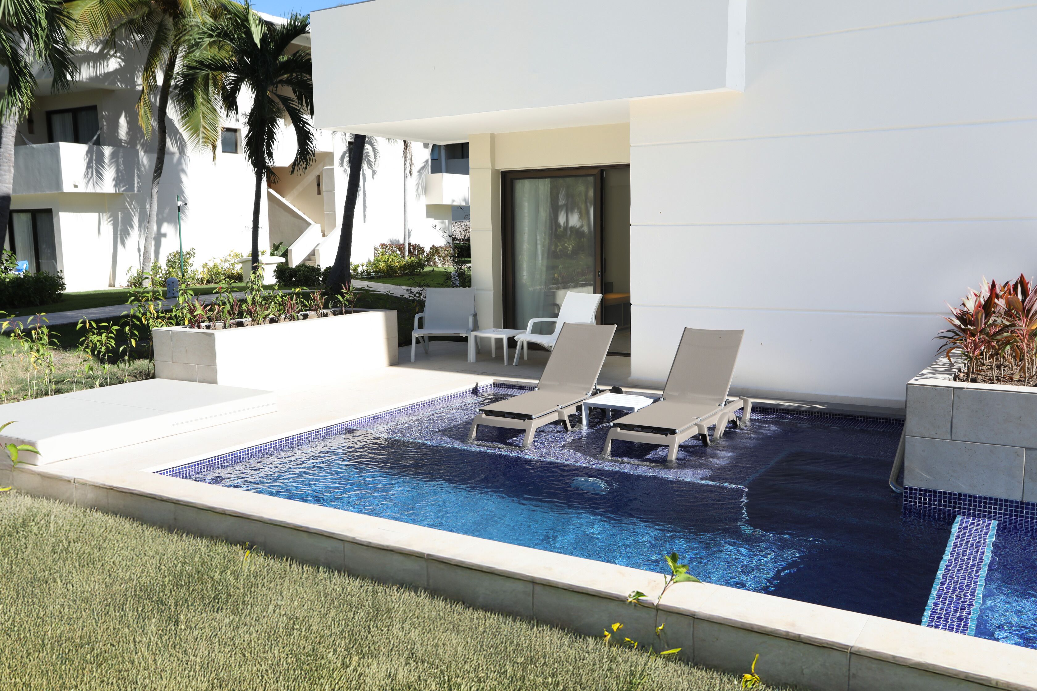 A swimming pool with lounge chairs, a small deck area, and a modern building in the background.