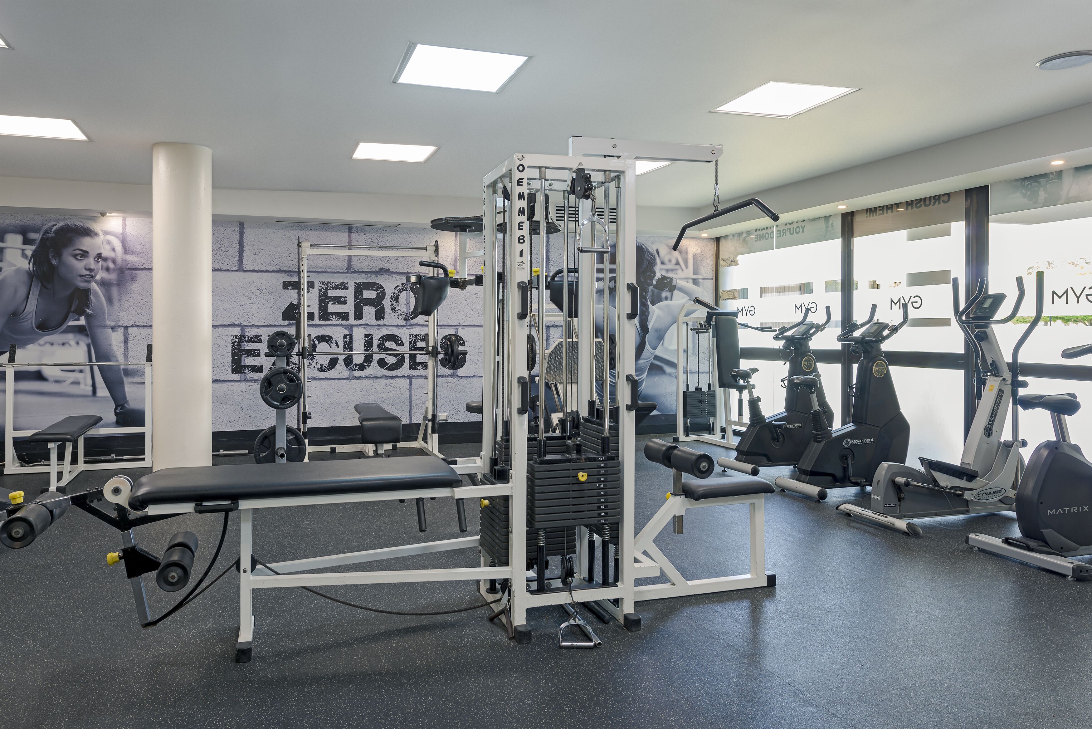 Ein Fitnessstudio mit verschiedenen Trainingsgeräten, darunter eine Hantelbank, Kraftgeräte und Cardiogeräte.