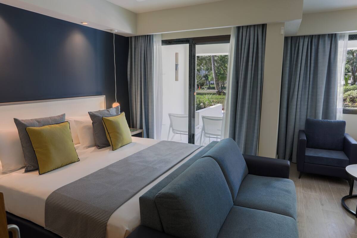 Ein Hotelzimmer mit Bett, Sofa, Sessel und Blick ins Freie.