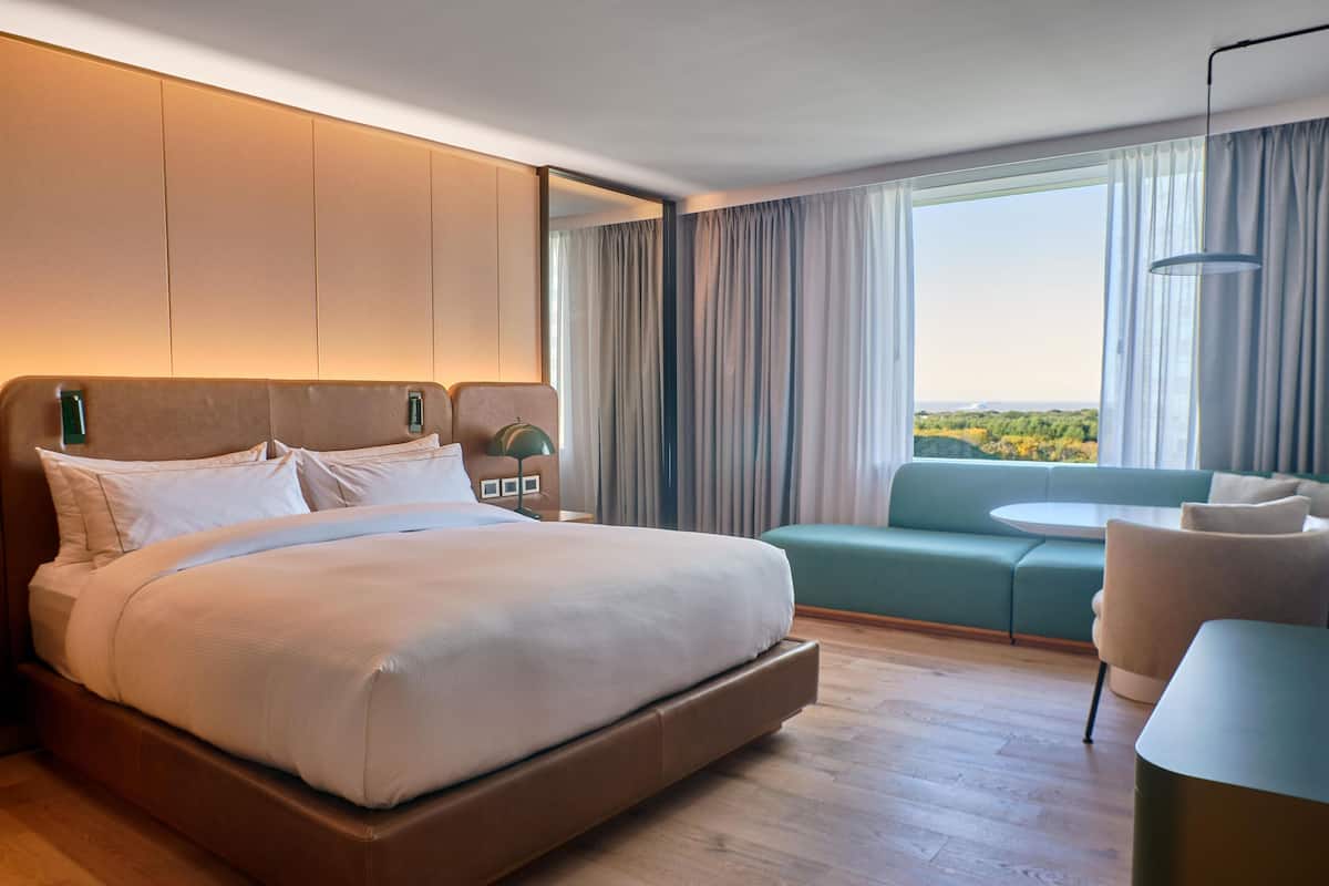 Ett modernt hotellrum med en stor säng, en soffa, ett litet bord och utsikt över omgivningarna.