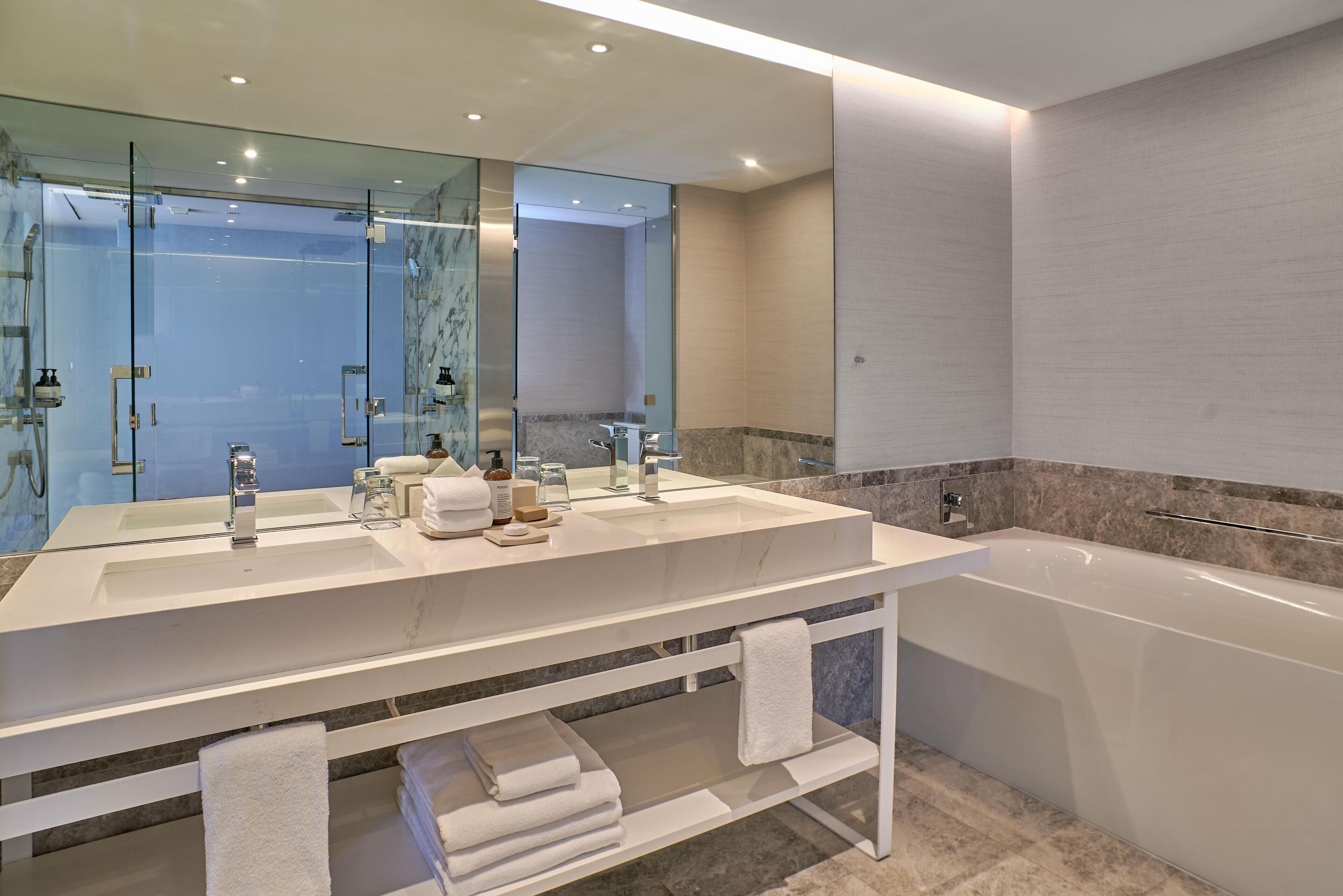 Un bagno moderno con uno specchio grande, due lavandini, una vasca e un box doccia in vetro.