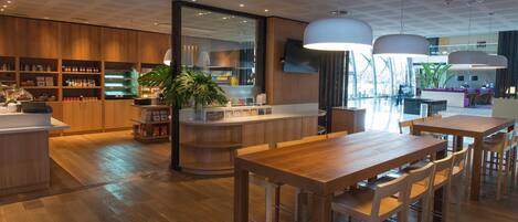 A modern hotel lobby with wooden flooring, a reception desk, a bar area, and seating arrangements.