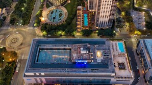 Un hotel moderno de gran altura con fachada de vidrio, piscina en la azotea y un patio ajardinado.