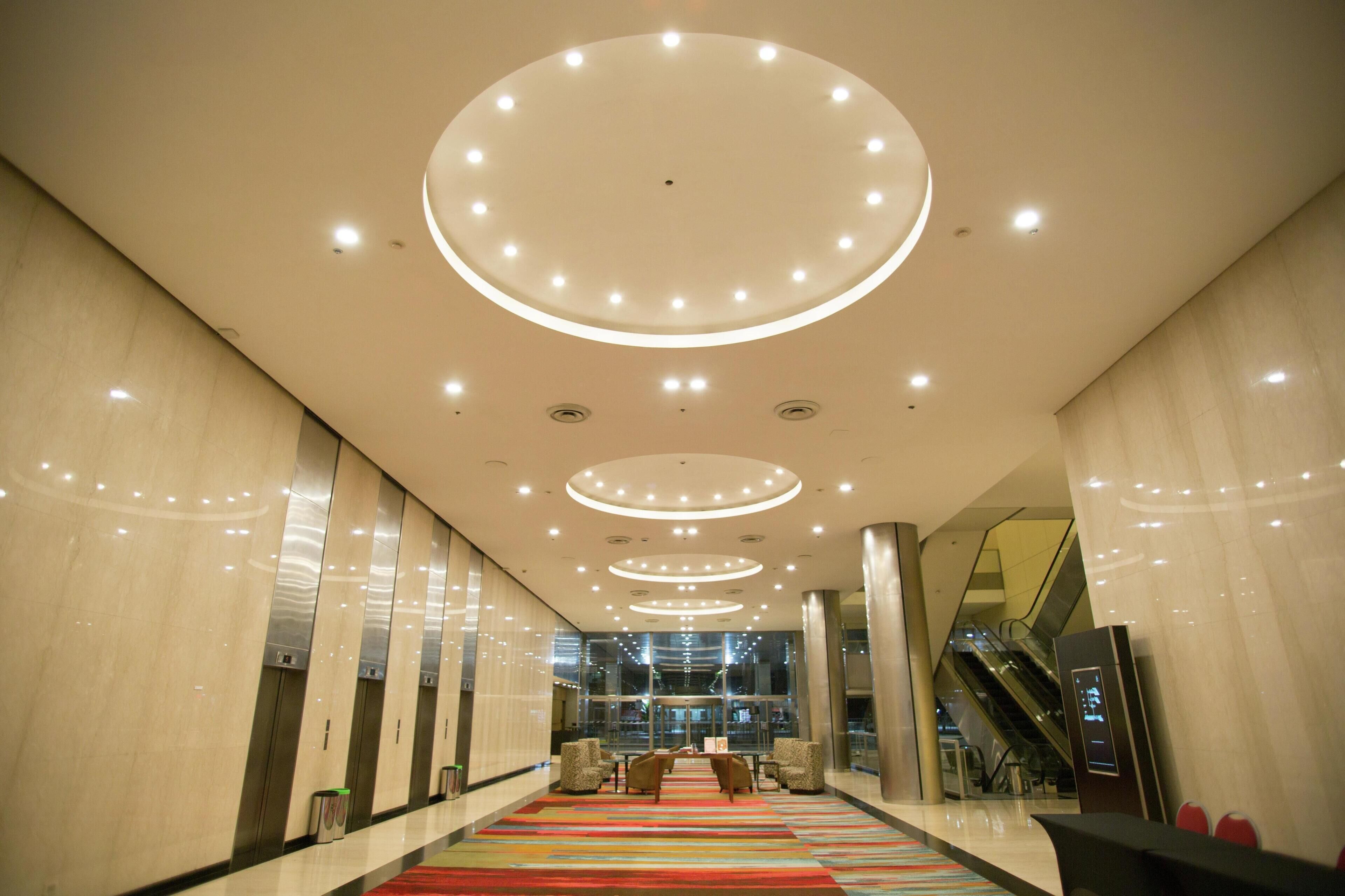 A modern lobby with a central seating area, multiple elevators, and a glass facade in the background.