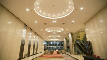 A modern lobby with a central seating area, multiple elevators, and a glass facade in the background.