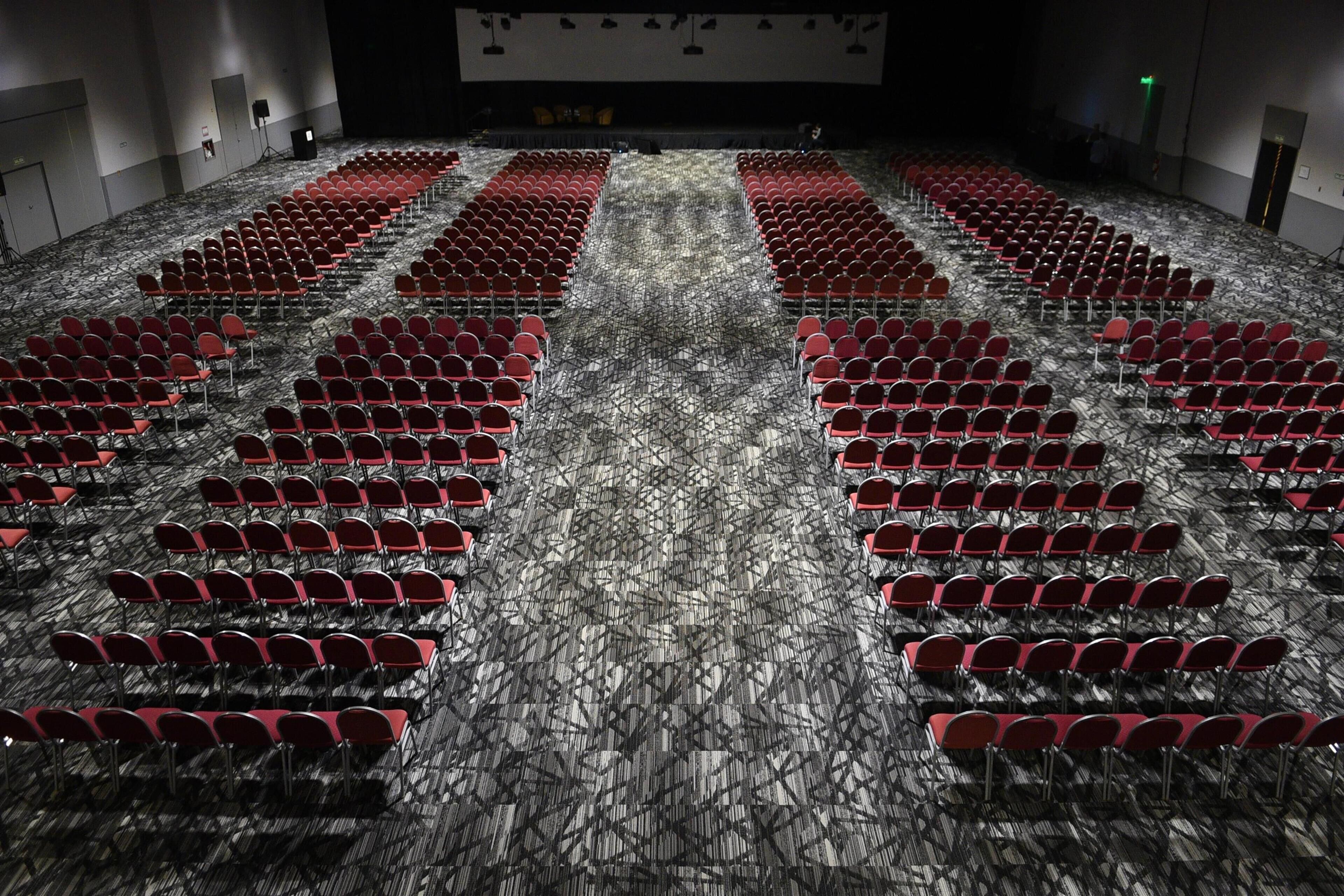 A large indoor auditorium with rows of red chairs and a patterned carpet.