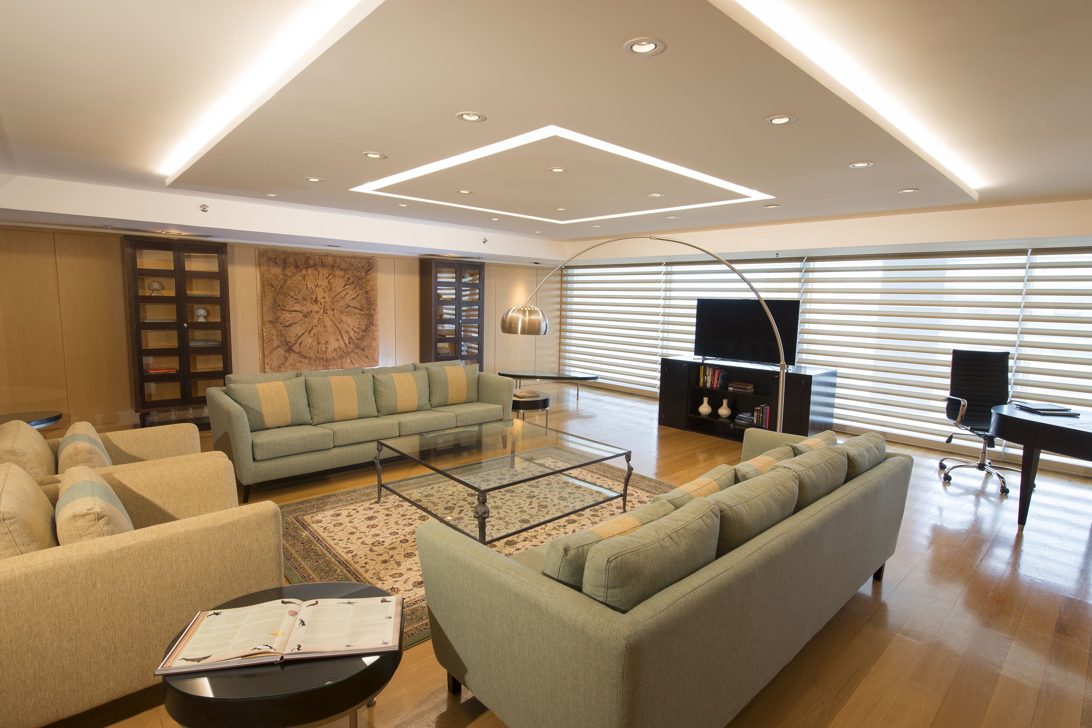 A spacious living room with a sectional sofa, a glass coffee table, and a modern ceiling design.