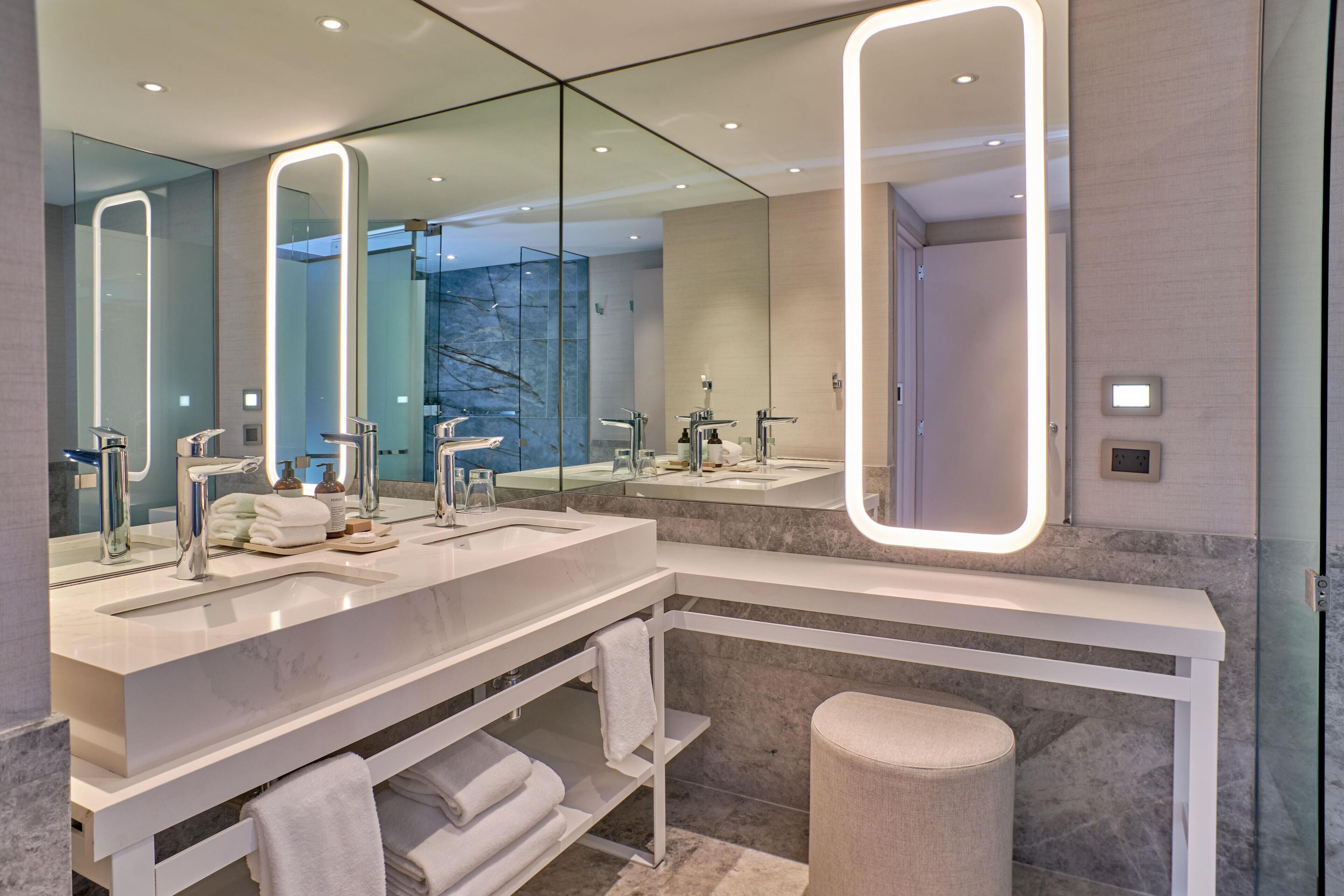 Un baño moderno con dos lavamanos, tocador y un espejo grande con iluminación integrada.