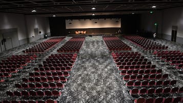 A large auditorium with rows of red chairs, a stage, and a carpeted floor.