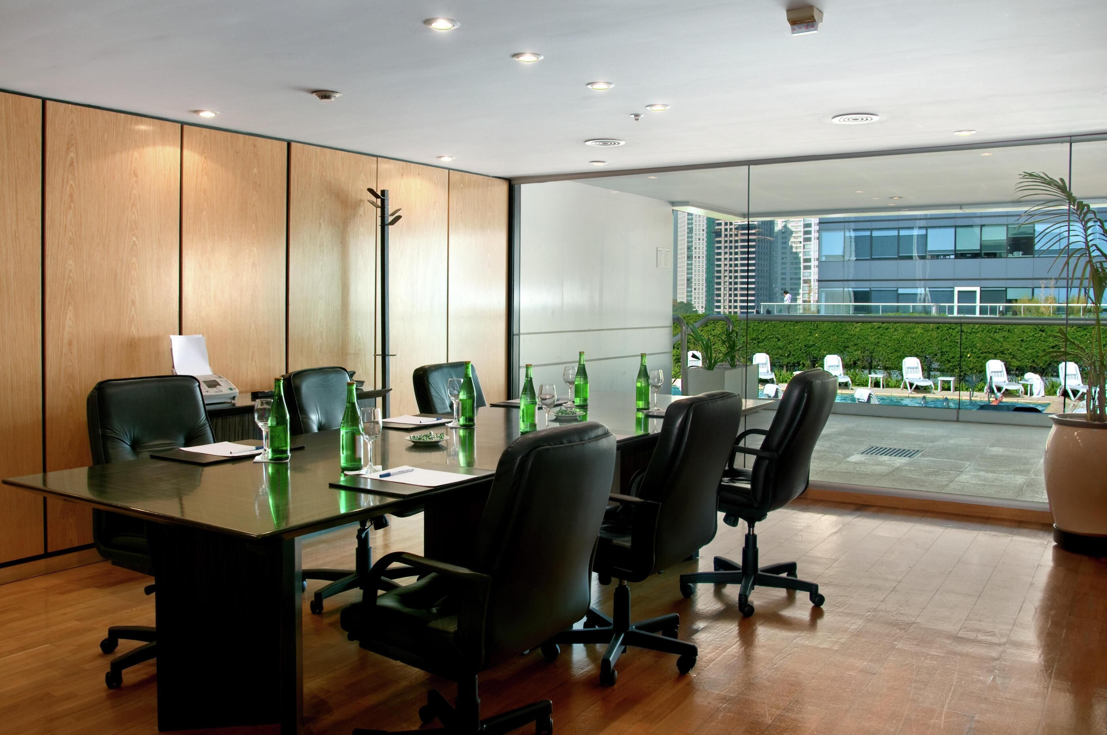 A conference room with a glass wall, wooden paneling, and a view of a building and greenery outside.