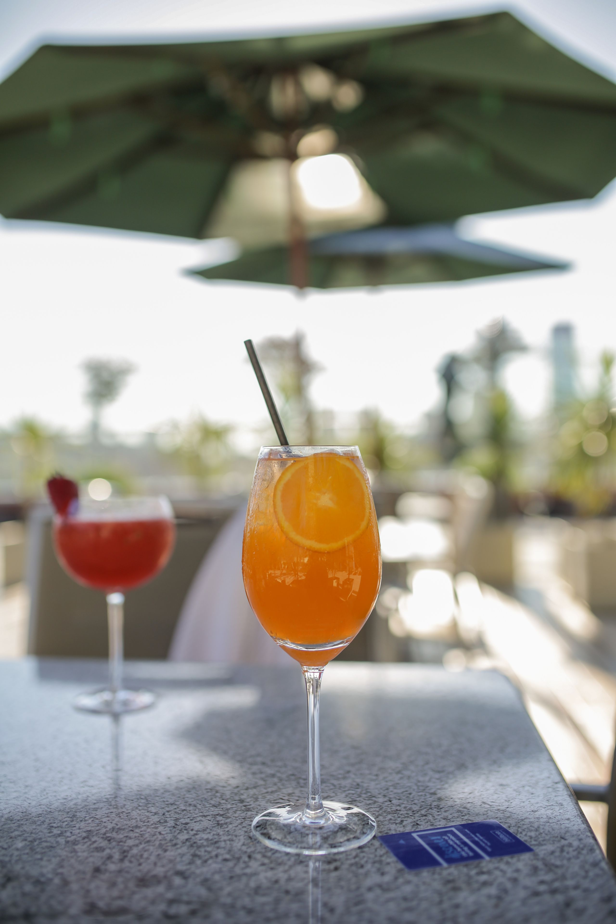 Two cocktails on a table with an umbrella in the background.