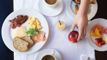 Una mesa de desayuno con platos de comida, tazas de café y una mano alcanzando una manzana.