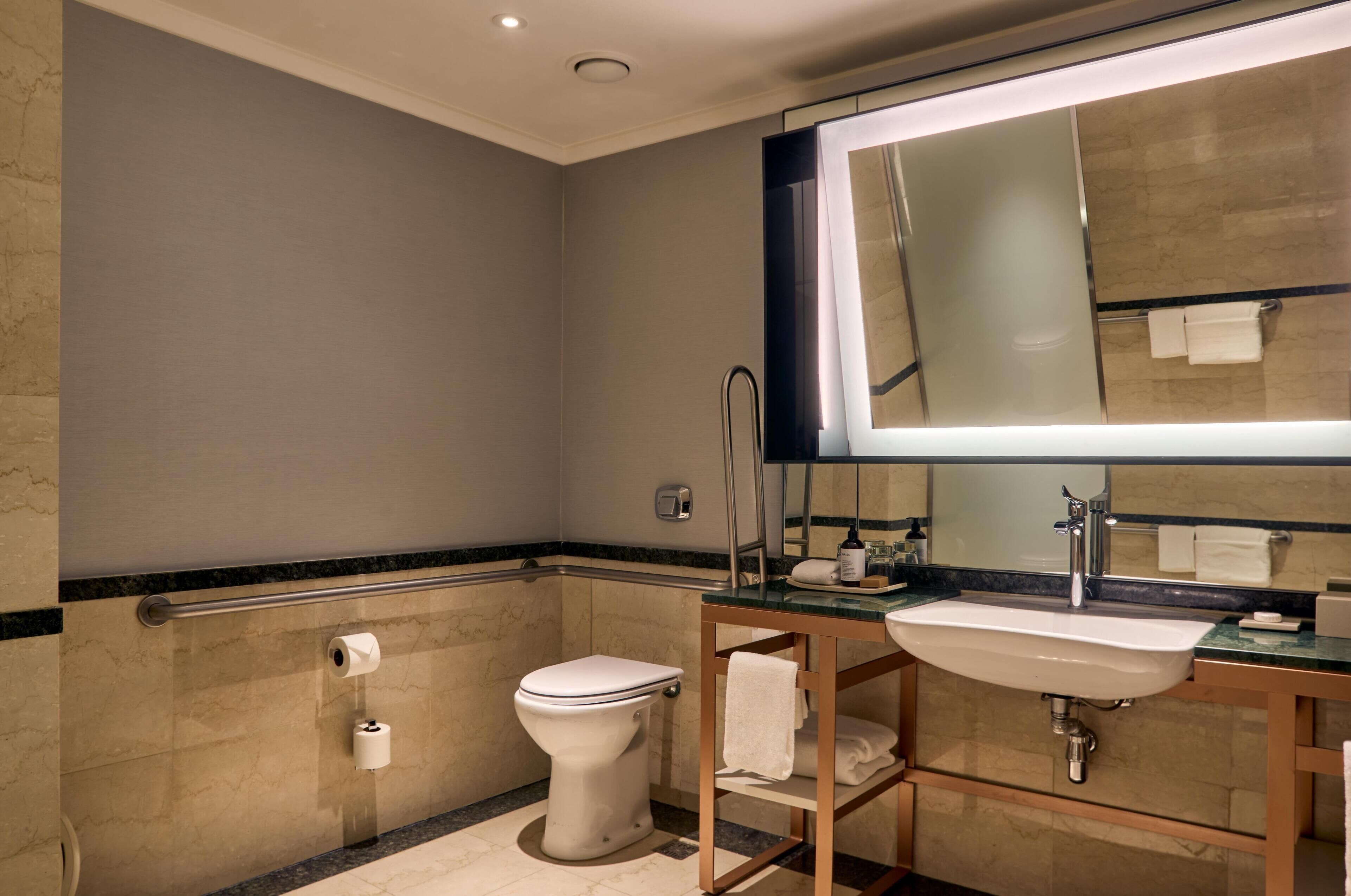 A modern bathroom with a toilet, sink, mirror, and towel rack.