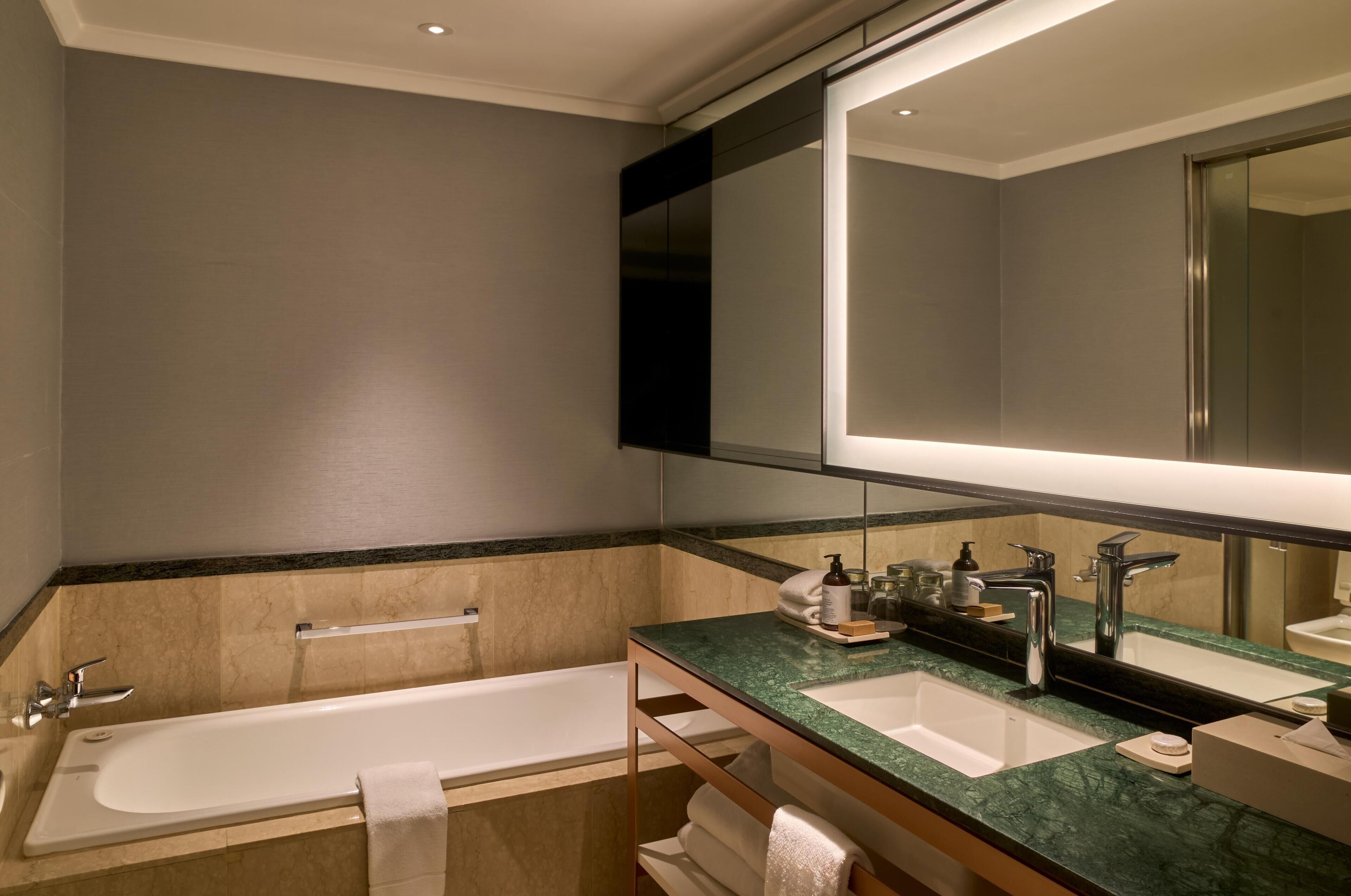 A modern bathroom with a bathtub, two sinks, a large mirror, and a towel rack.