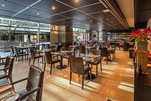 Un restaurant spacieux, doté de nombreuses tables et chaises, de grandes fenêtres et d’un espace extérieur bien visible où l’on peut s’asseoir.