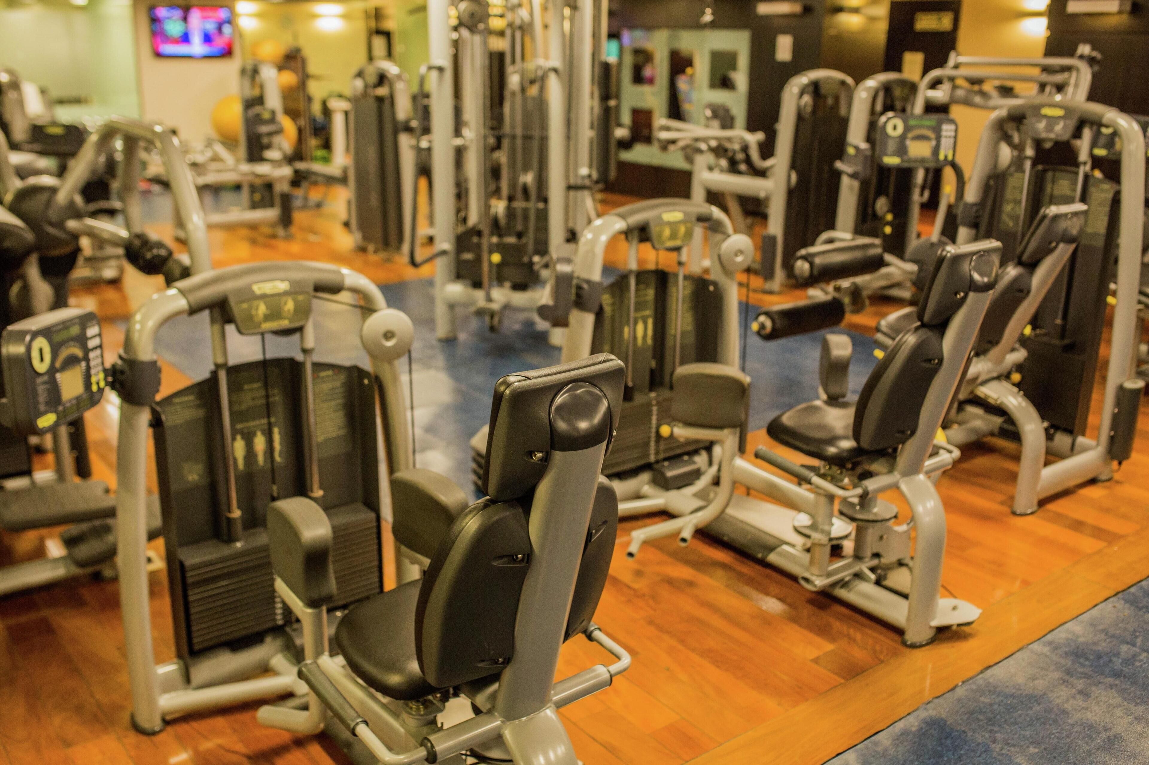 Een fitnessruimte met diverse trainingsapparaten en een televisiescherm op de achtergrond.