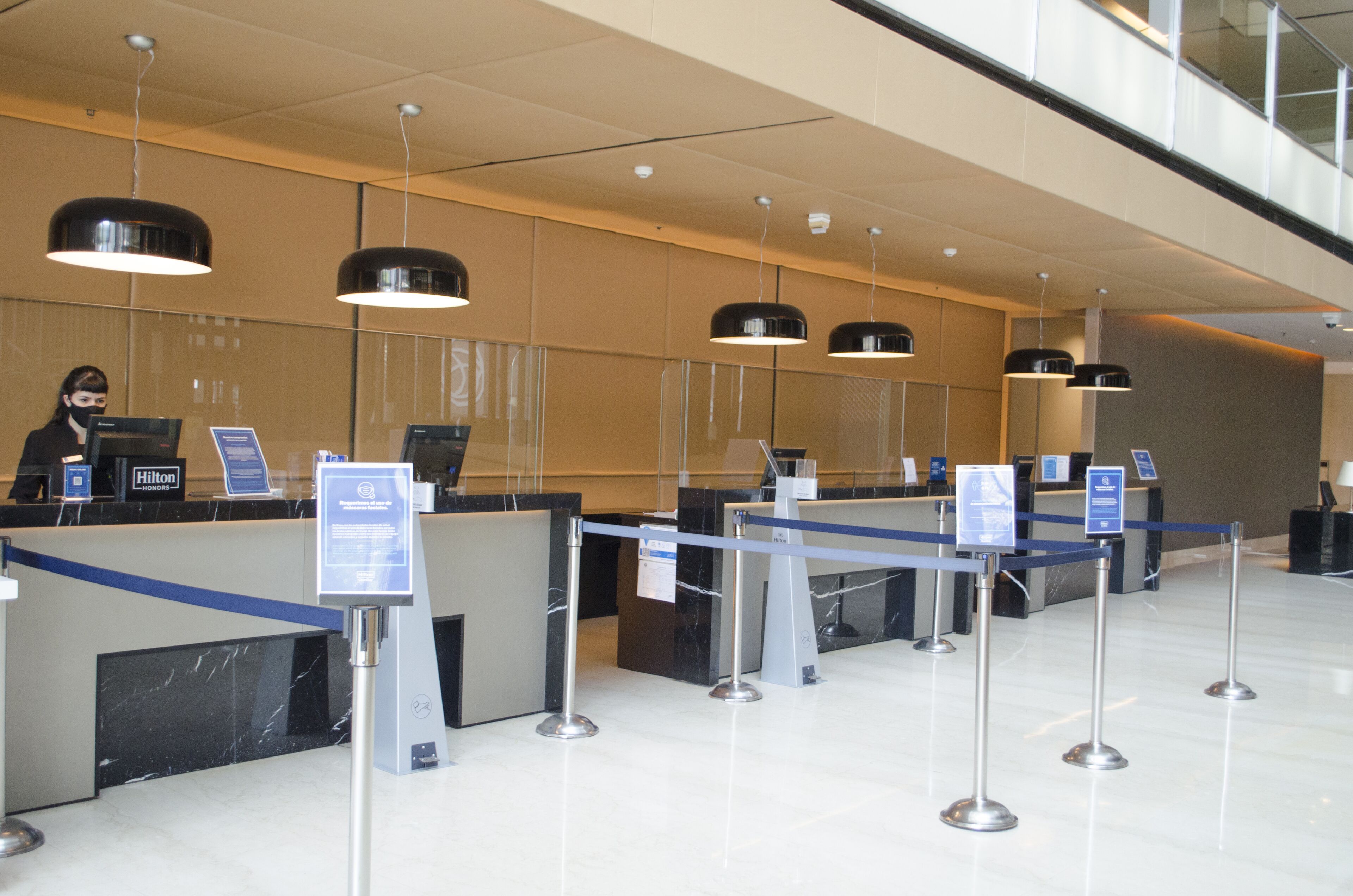A hotel reception area with a marble counter, black and white pendant lighting, and a glass railing overlooking the lobby.